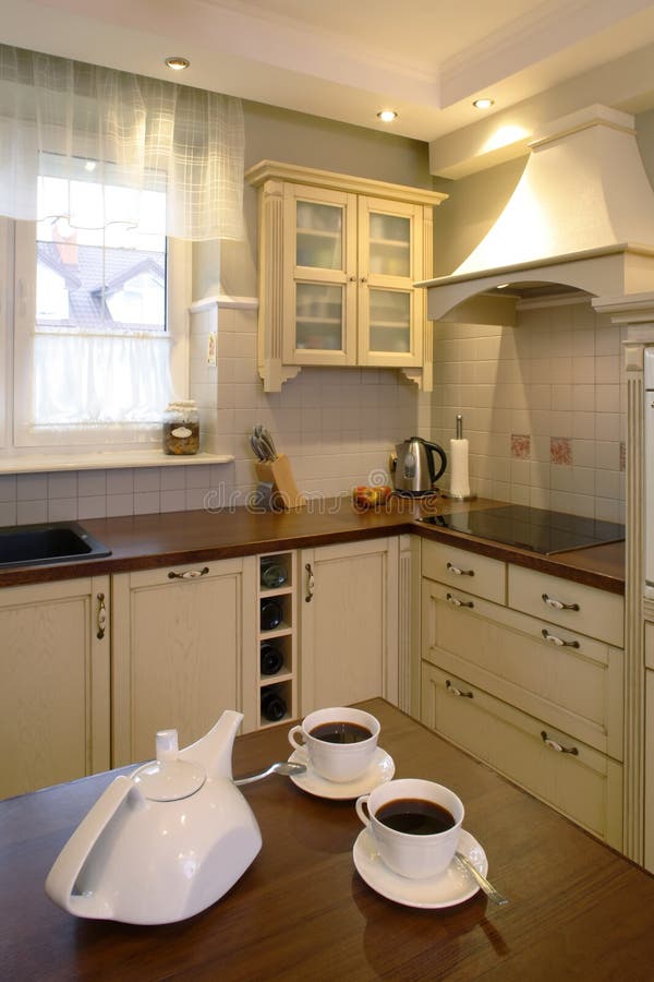 Classic Kitchen And Tea. Classic streamline kitchen area of a home. White teapot and two cups of tea are sitting on the counter in foreground of picture stock photography