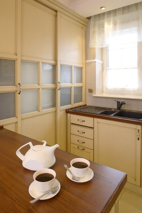 Classic Kitchen with Teapot And Cups. Classic streamline kitchen area of a home. White teapot and two cups of tea are sitting on the counter stock photography