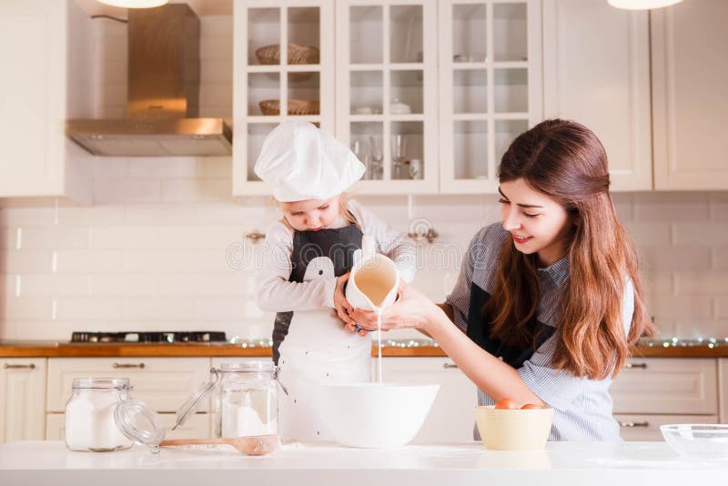 The little daughter in the chef`s hat and apron and her mother prepare baking in the bright, classic kitchen. Mothers Day royalty free stock photo